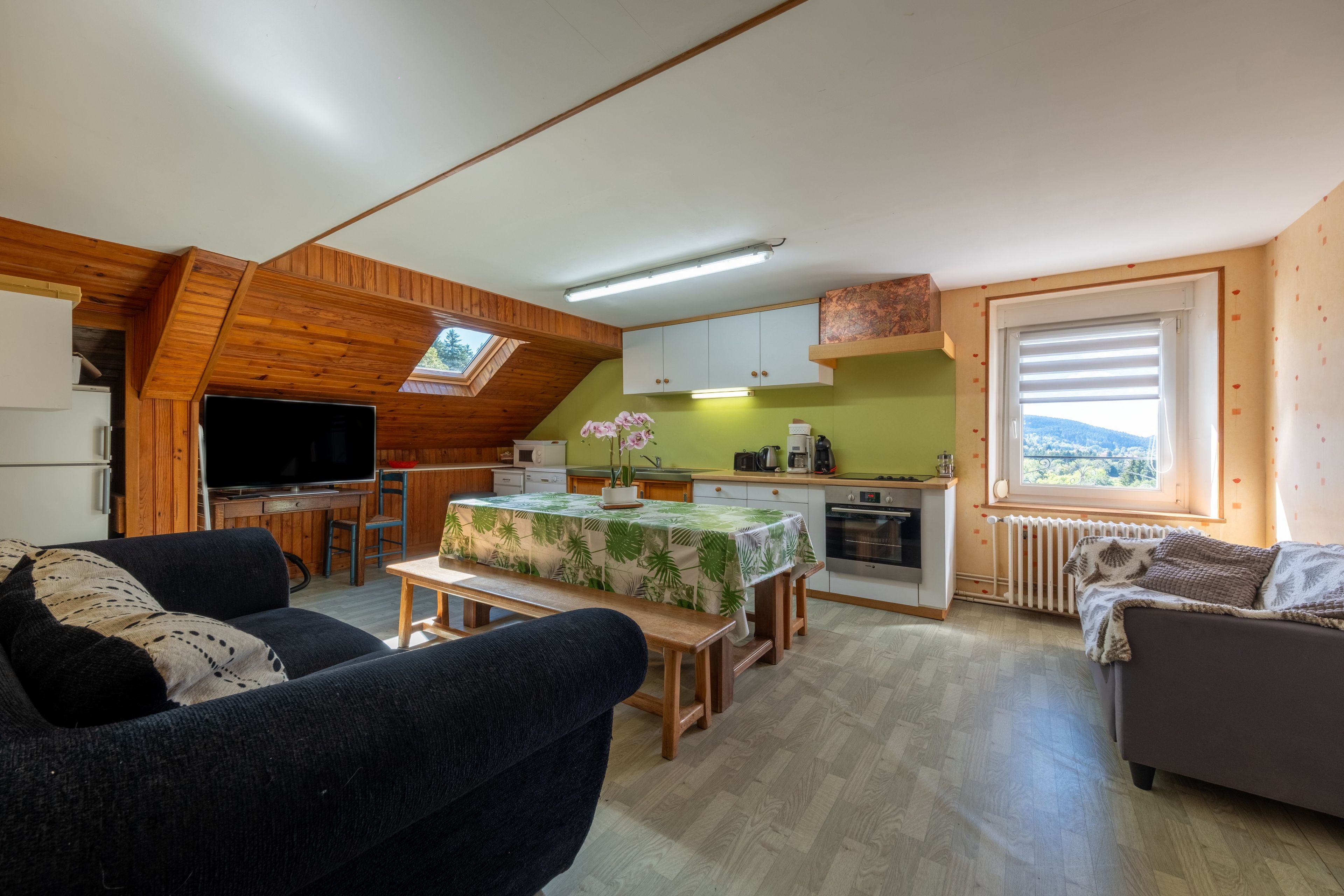 A cozy living room with a television, a sofa, and a dining area with a table.