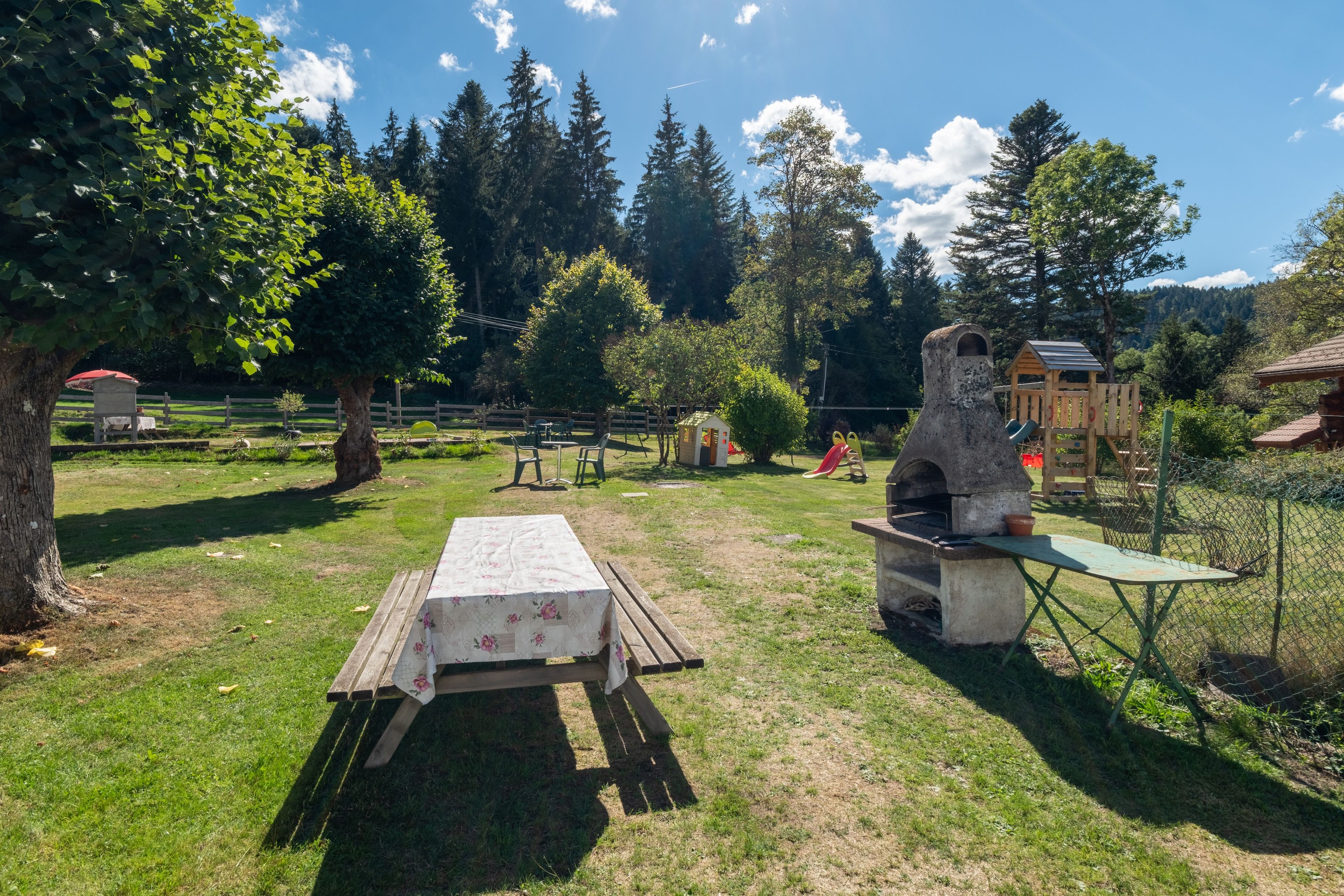 Een terras buiten met een tafel, stoelen, een barbecue en een speelconstructie.