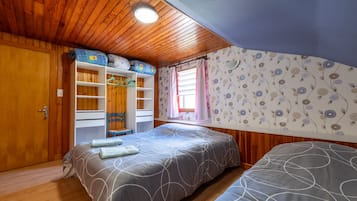 Ein Schlafzimmer mit Holzboden, einem Bett mit grau gemustertem Bettbezug, einem Kleiderschrank und einem Fenster mit floralem Wandpapier.
