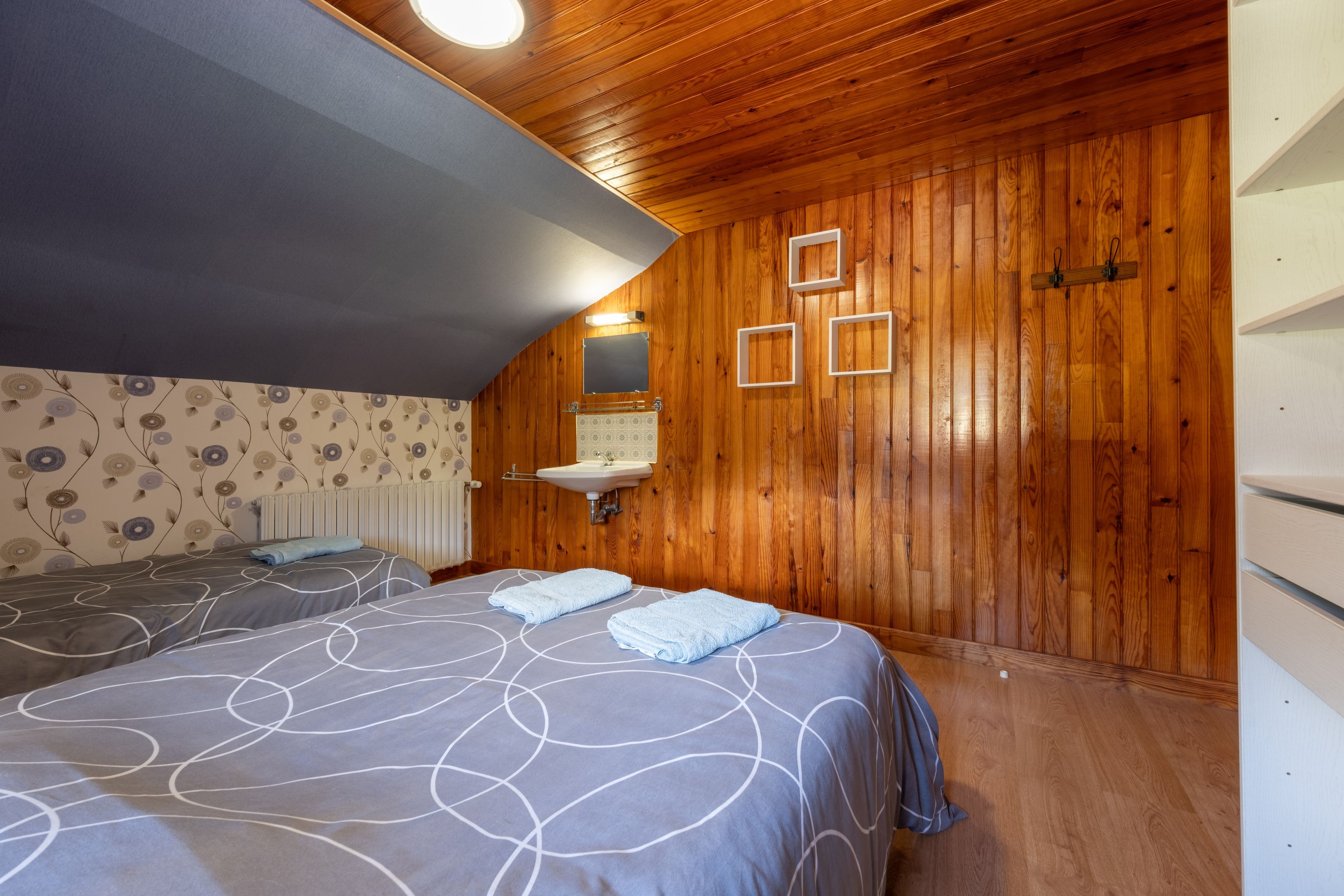 A bedroom with two beds, a wooden ceiling, a wall-mounted sink, and a radiator.