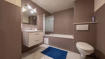 Une salle de bain avec des toilettes blanches, un lavabo avec un miroir et un tapis de bain bleu.