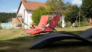 Outdoor lounge chairs and a wooden play structure in a grassy yard with a house in the background.