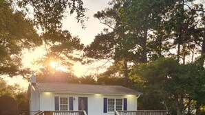 A two-story house with a gravel driveway, wooden deck, and a fenced yard. - Charming 2-bedroom house in Oak Island close to the beach (Oak Island)
