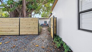 Un edifici modern amb una entrada de grava, una tanca de fusta i una casa al fons.