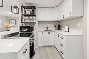 A modern kitchen with white cabinetry, a built-in microwave, a stove, and a sink. - Perfect stay for 2-Walk to Wilton Drive-Shops &bars (Wilton Manors)