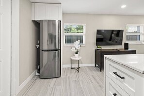A modern kitchen with a stainless steel refrigerator, a small white table with a potted orchid, a dark wooden cabinet, and a white countertop. - Perfect stay for 2-Walk to Wilton Drive-Shops &bars (Wilton Manors)