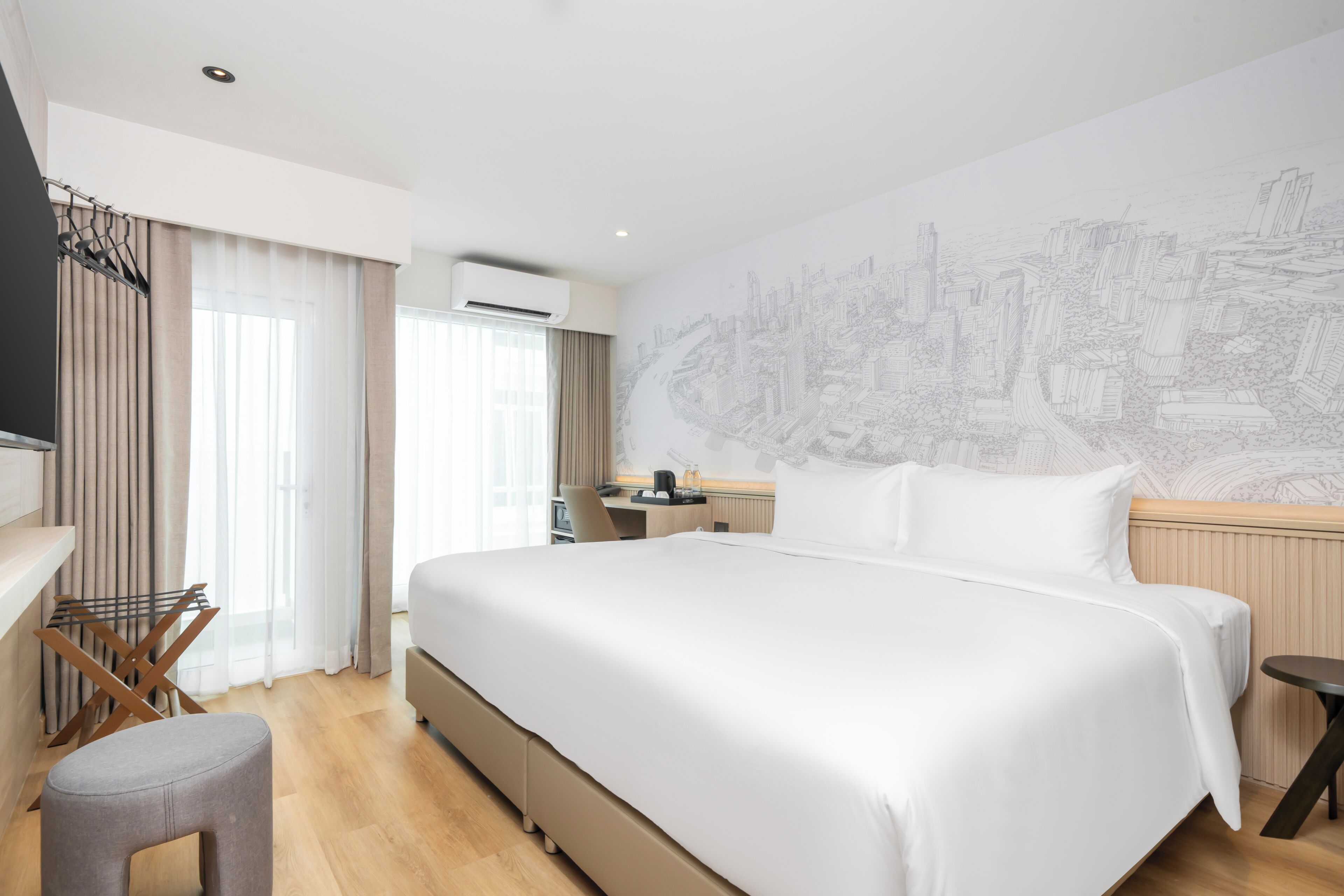 A hotel room with a large bed, a desk, a chair, and a wall-mounted TV.