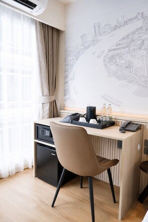 Habitación de hotel con escritorio, una silla, cafetera, teléfono y un mural urbano en la pared.