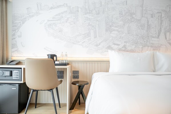 A hotel room with a bed, a desk with a chair, a small table, and a large window with a cityscape view.