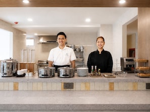 A commercial kitchen with stainless steel appliances, a buffet setup with food containers, and a coffee machine. - Surestay By Best Western Siriraj Bangkok (Bangkok)
