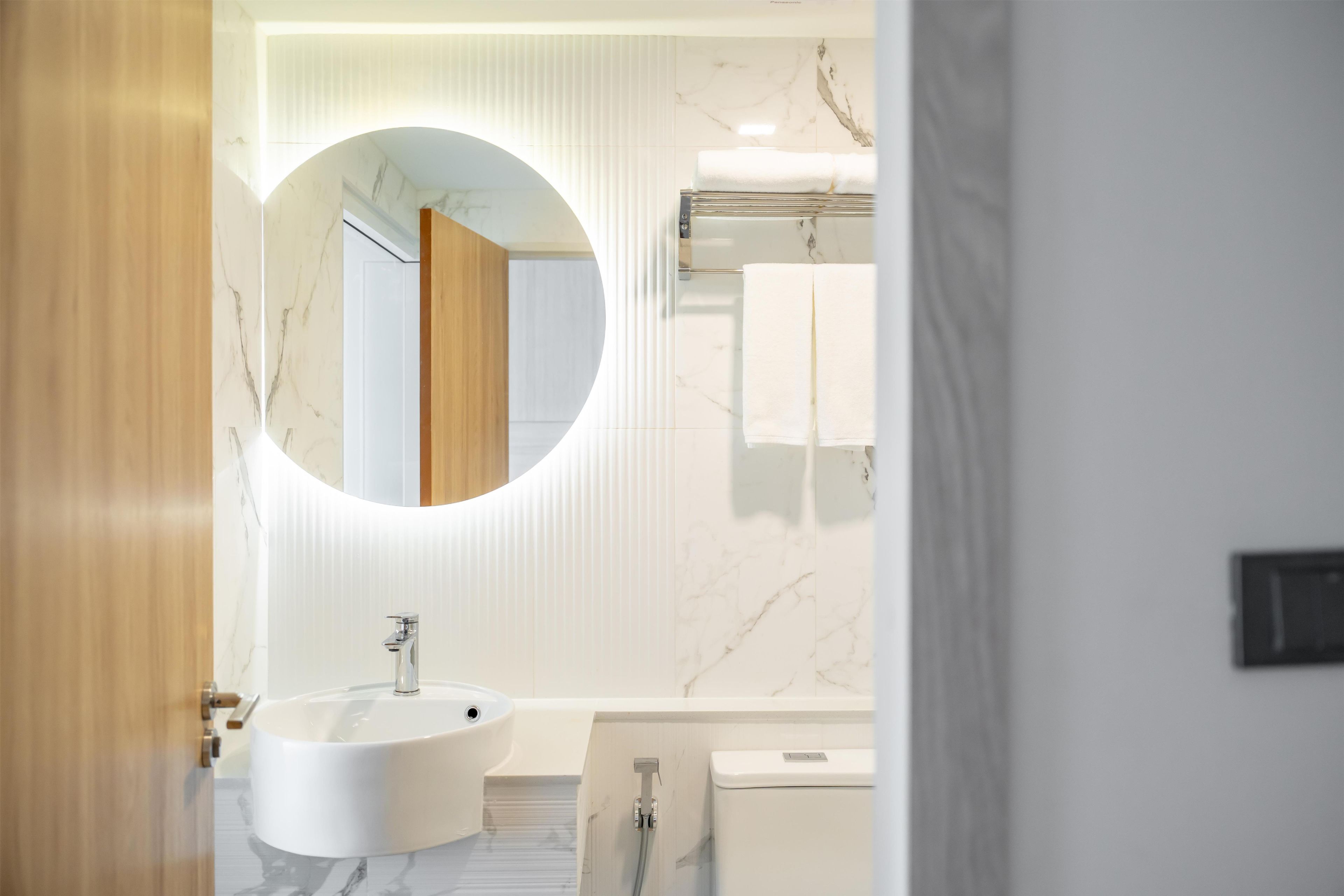 Une salle de bain moderne avec un grand miroir rond, une baignoire sur pieds et des toilettes.
