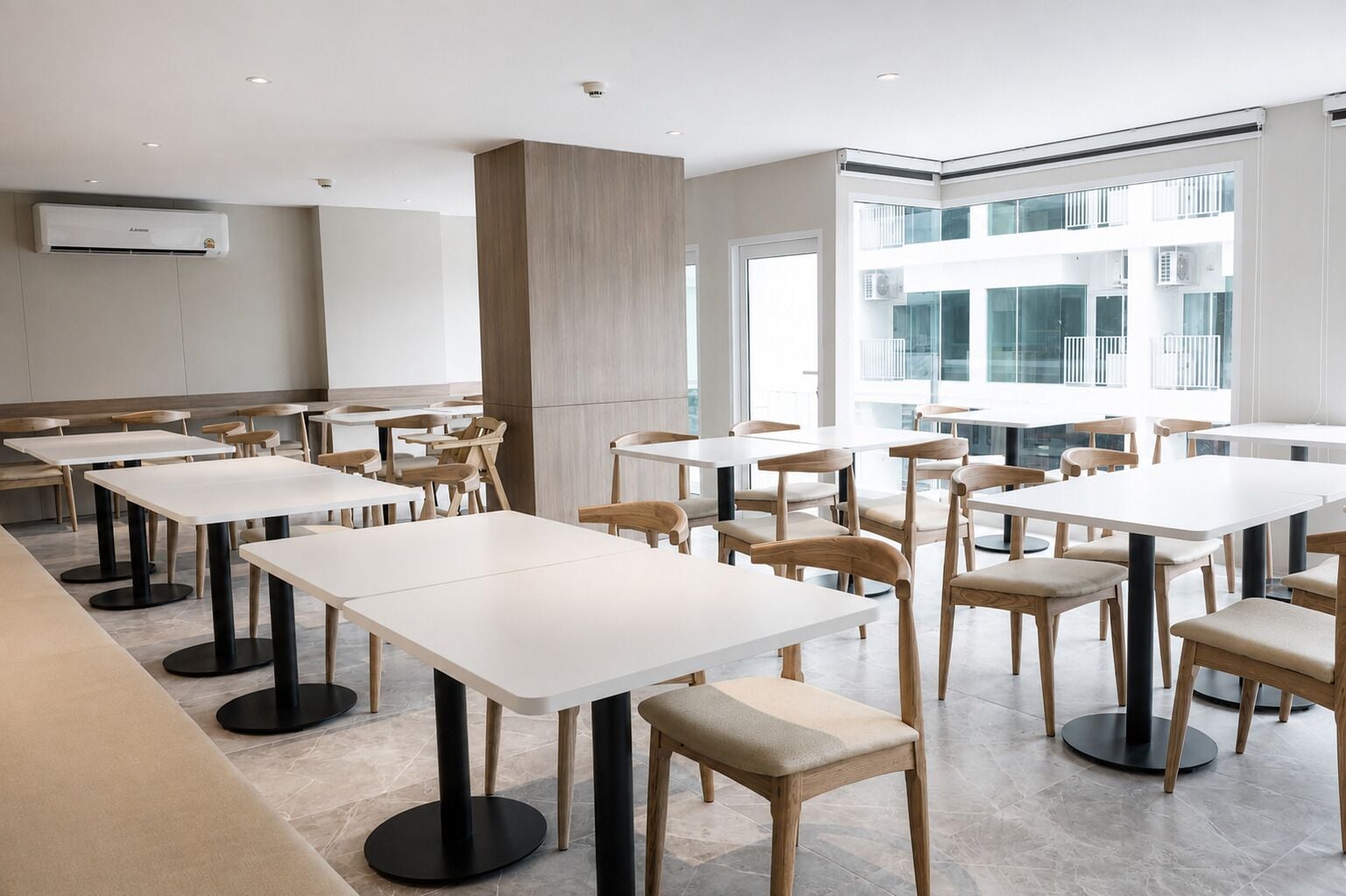 A modern dining area with white tables and chairs, a central pillar, and large windows.