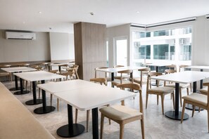A modern dining area with white tables and chairs, a central pillar, and large windows.