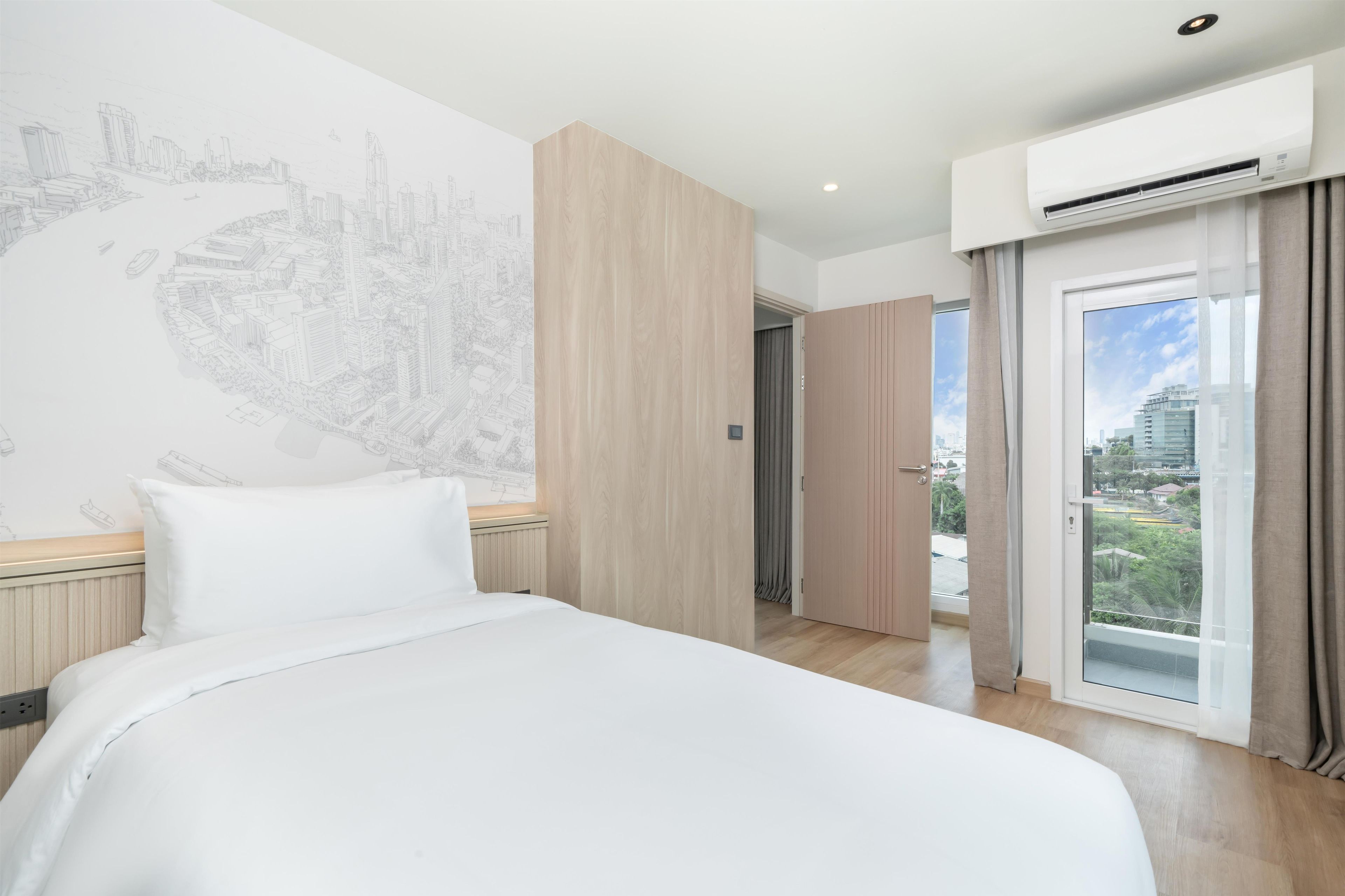 A hotel room with a large bed, a cityscape mural, a wardrobe, and a balcony with a view.