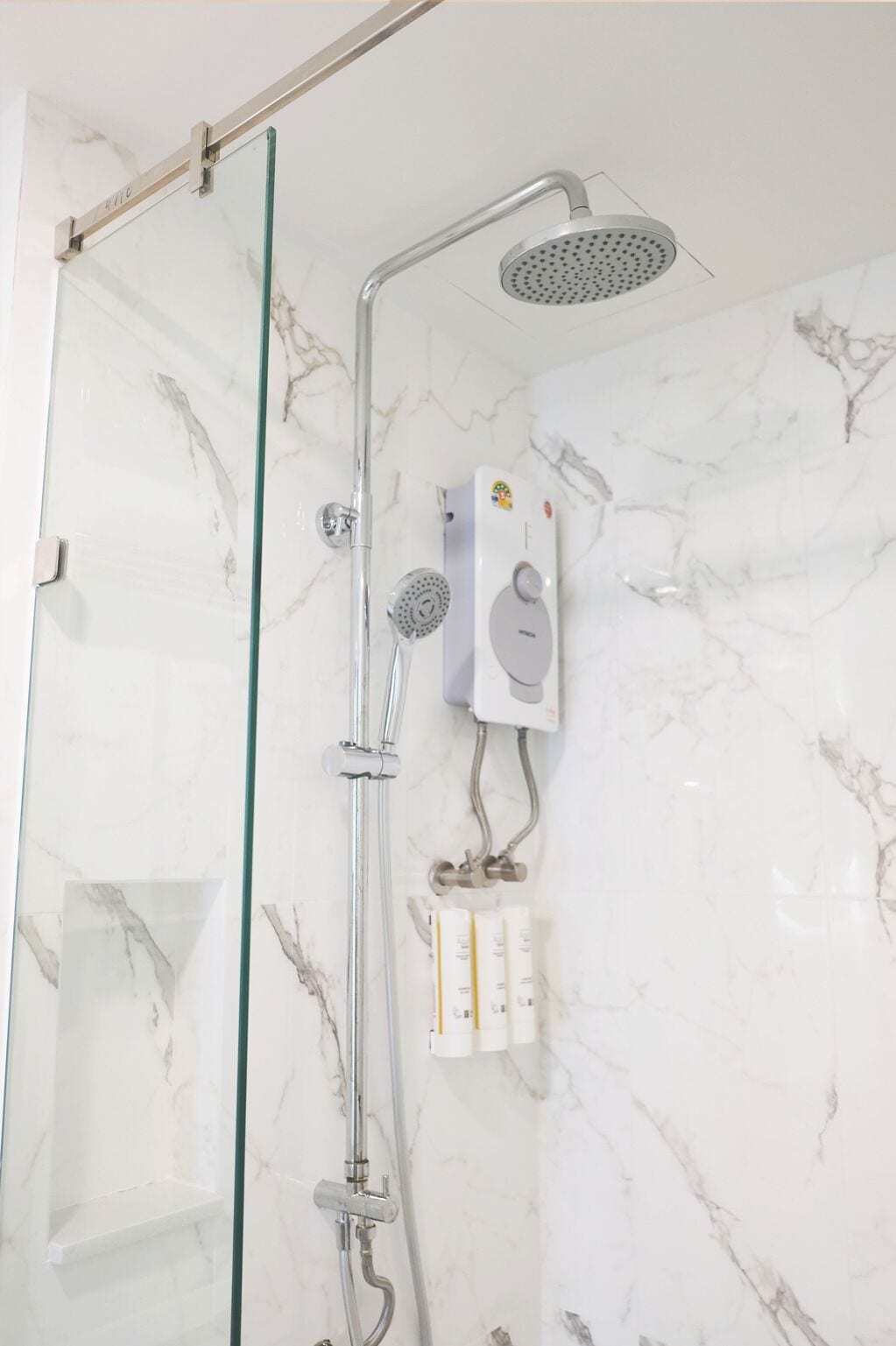 A shower area with a glass door, a handheld showerhead, a wall-mounted control panel, and a handheld showerhead.