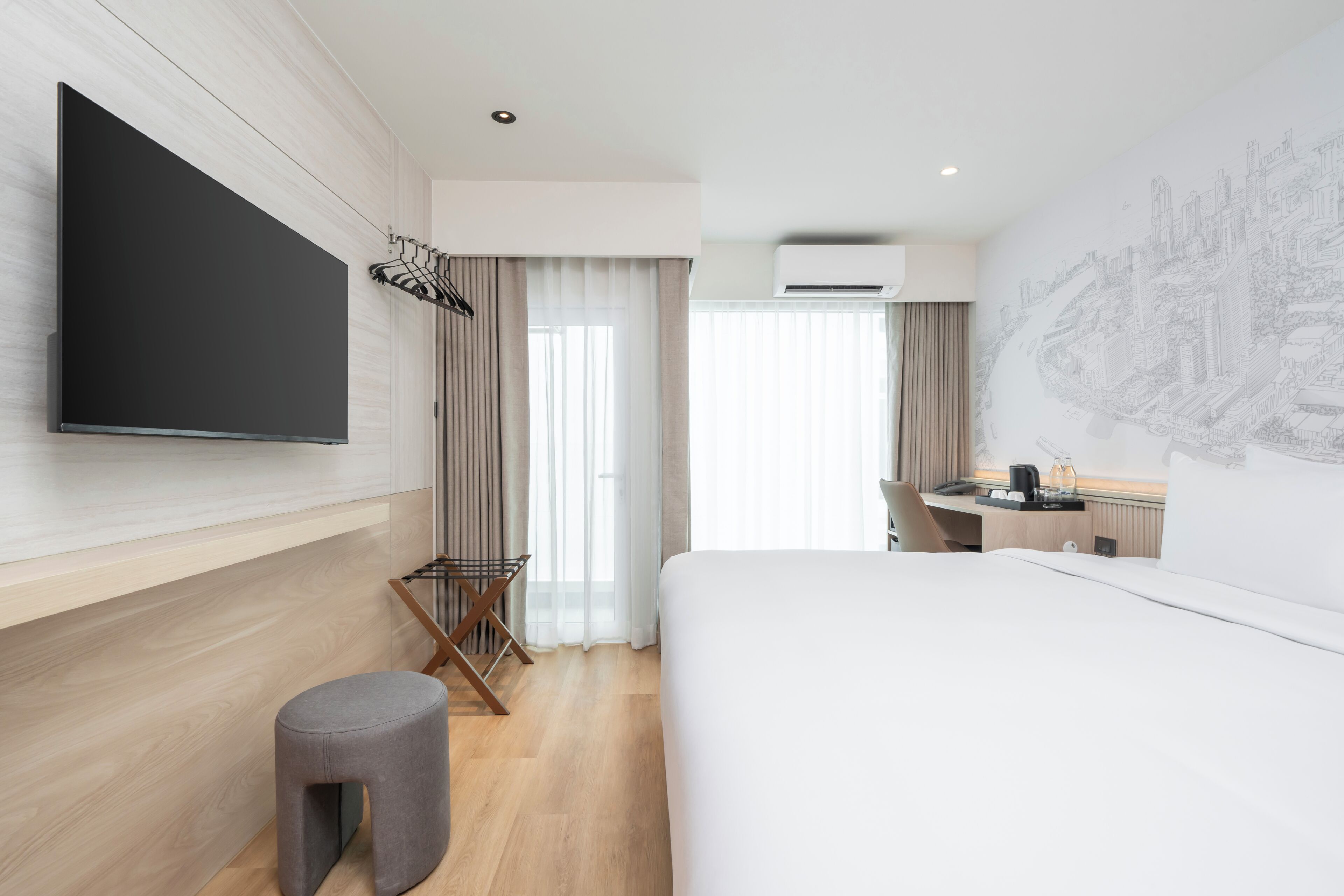 A modern hotel room with a flat-screen TV, a bed, a desk with a chair, and a large window with curtains.