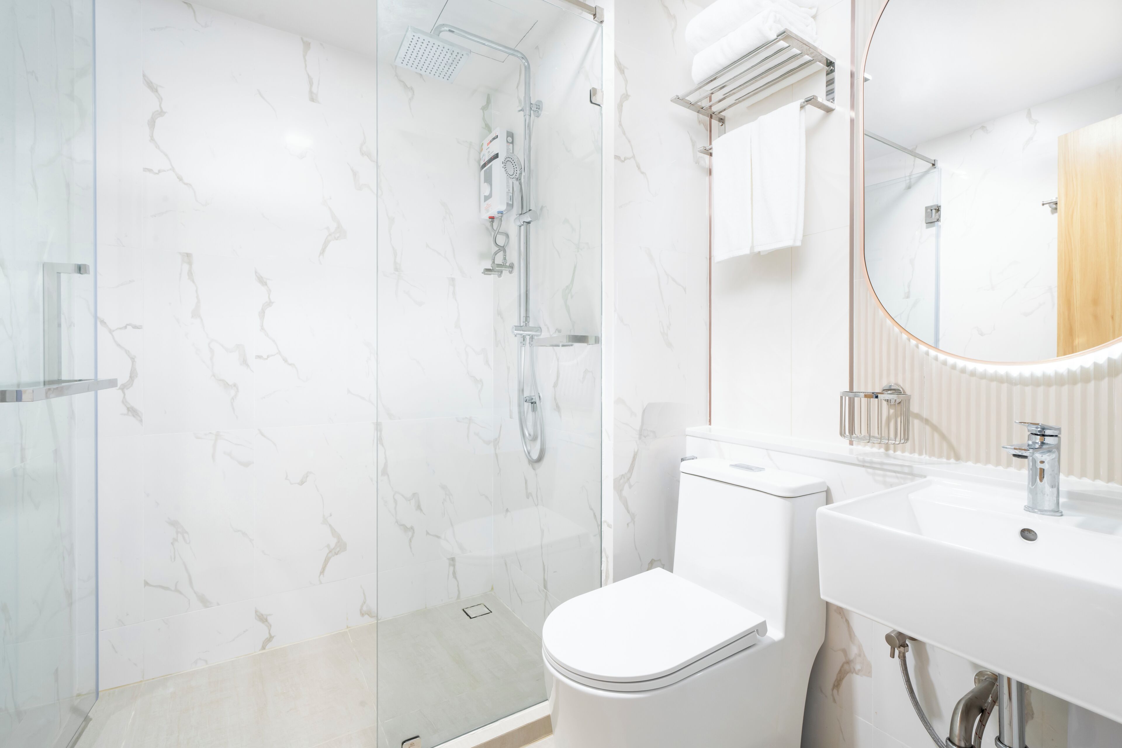 Un baño moderno con ducha envuelta en vidrio, inodoro blanco y lavamanos con espejo.