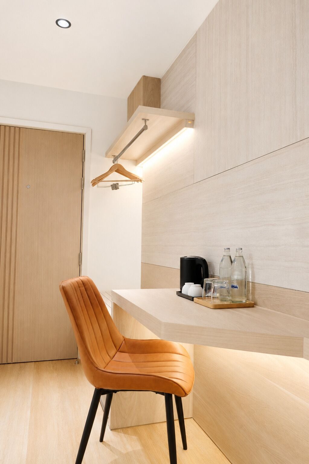 A modern room with a wooden door, a wooden chair, a shelf with a coffee maker, glasses, and bottles.