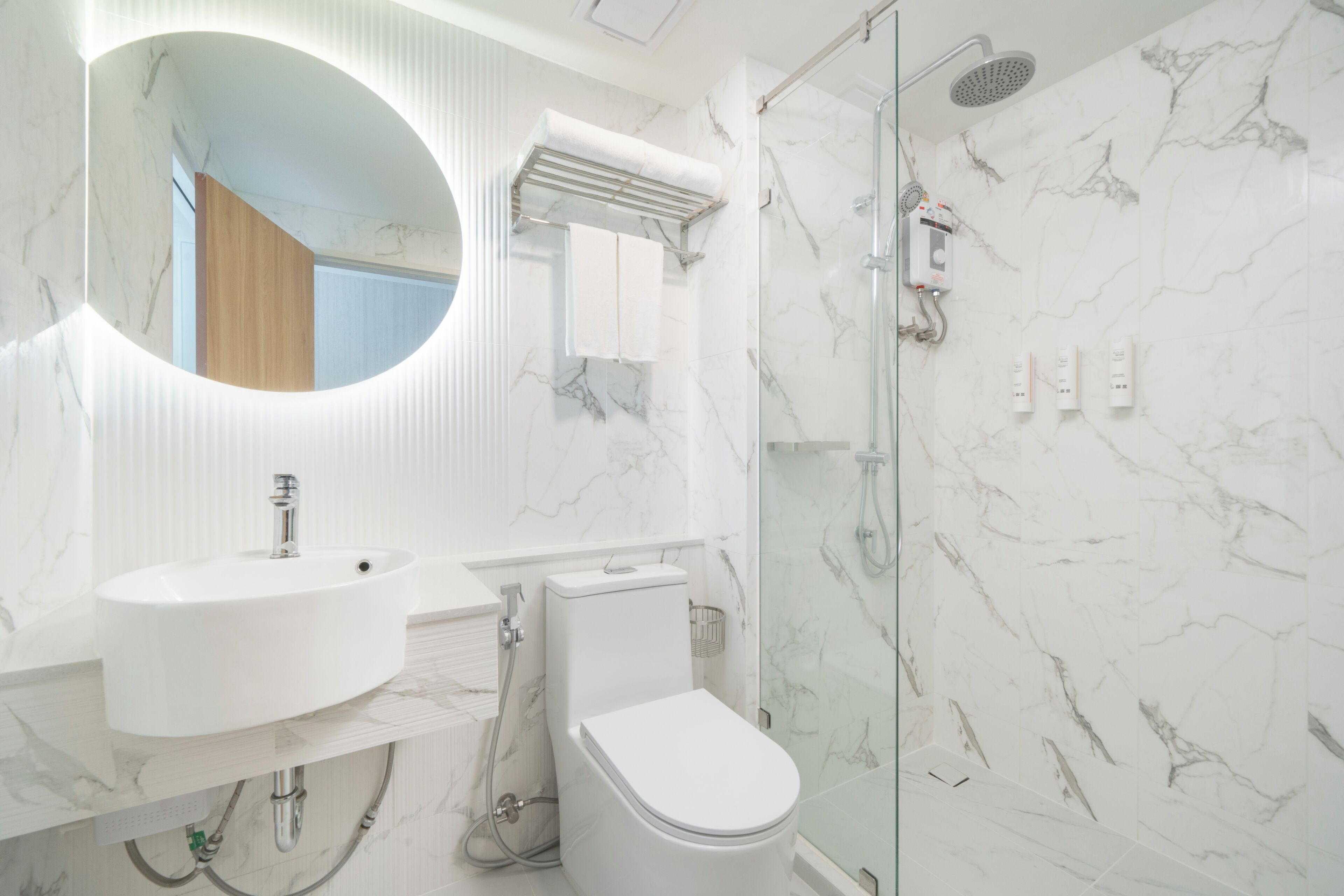A modern bathroom with a round mirror, a sink, a toilet, and a glass-enclosed shower area.