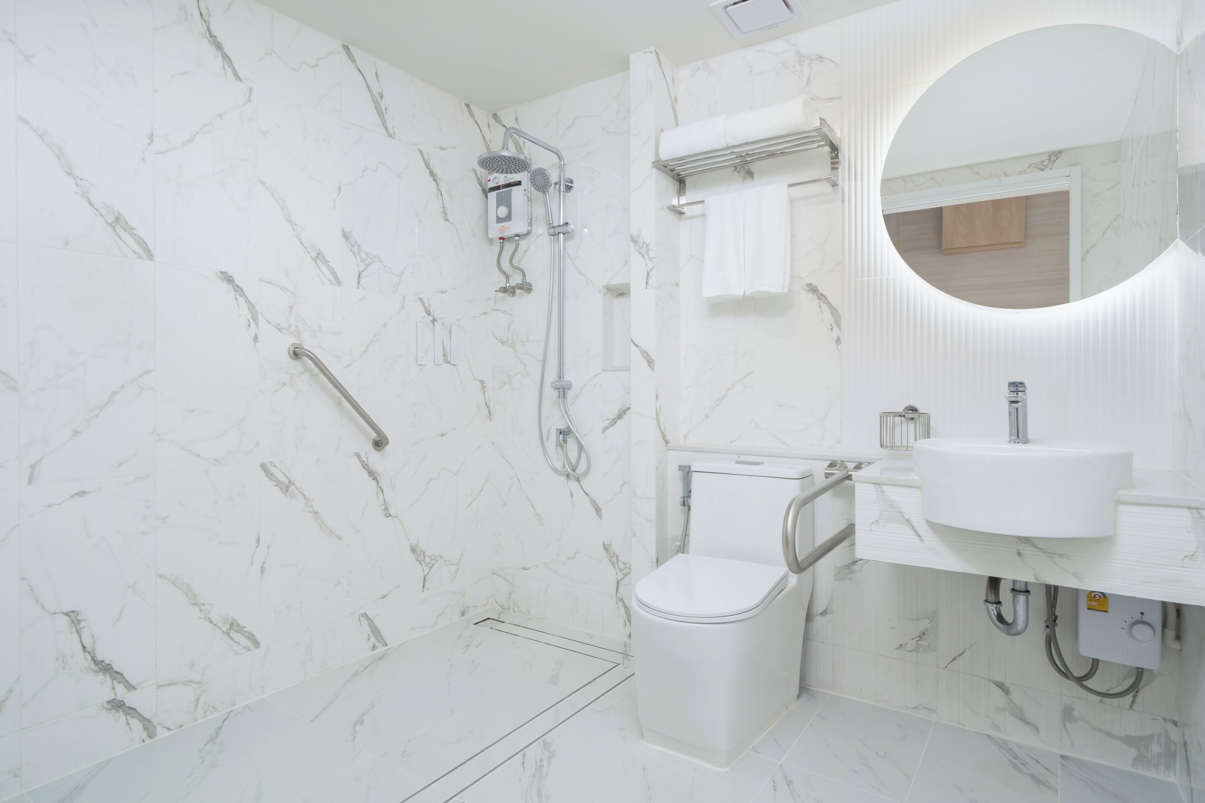 A modern bathroom with a marble wall, a toilet, a shower, and a sink with a mirror.