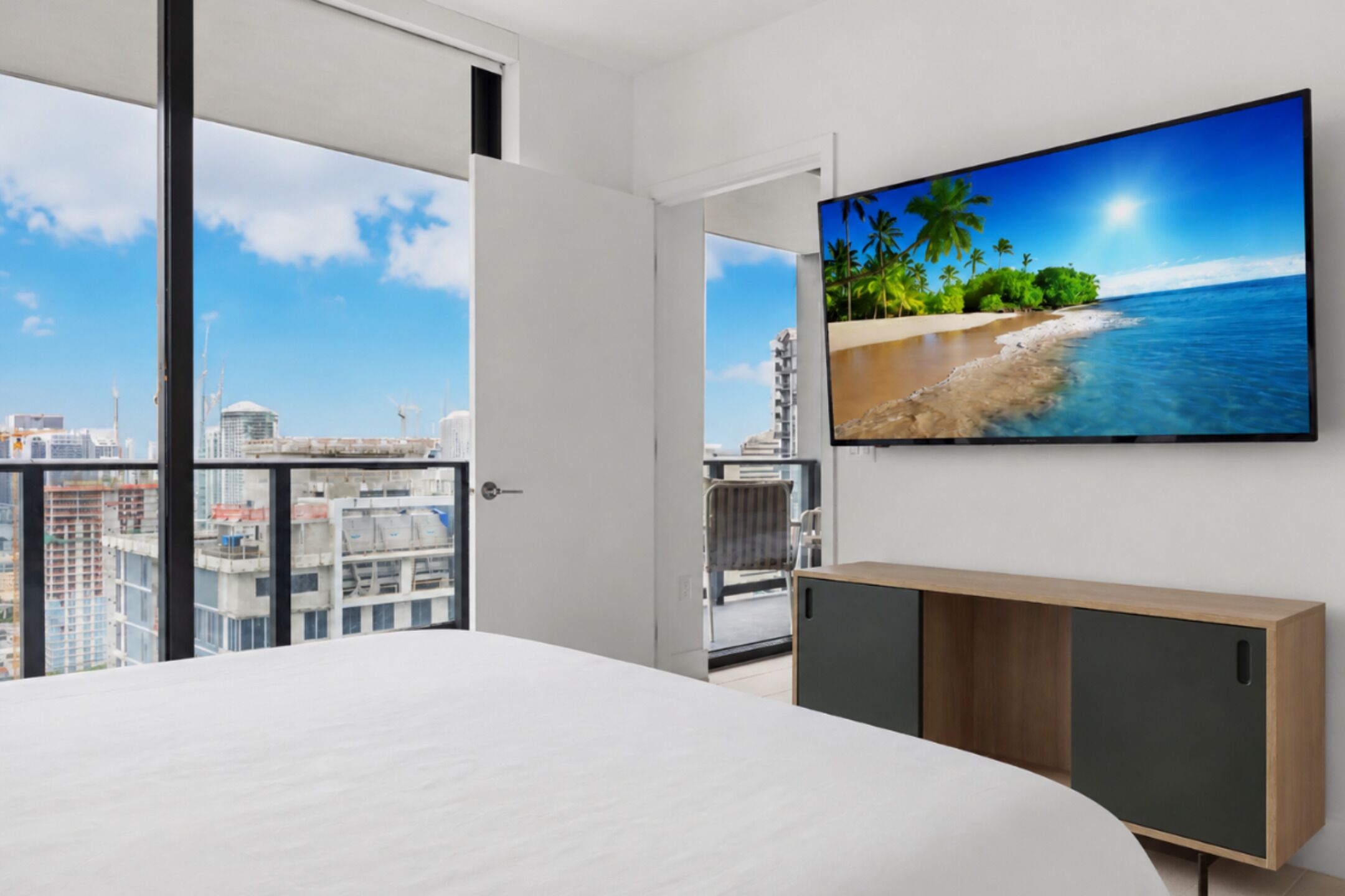 Una camera d'hotel moderna con un letto grande, una TV a parete e un balcone con vista sulla città.