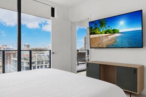 Une chambre d’hôtel moderne avec un grand lit, un téléviseur fixé au mur et un balcon offrant une vue sur la ville.