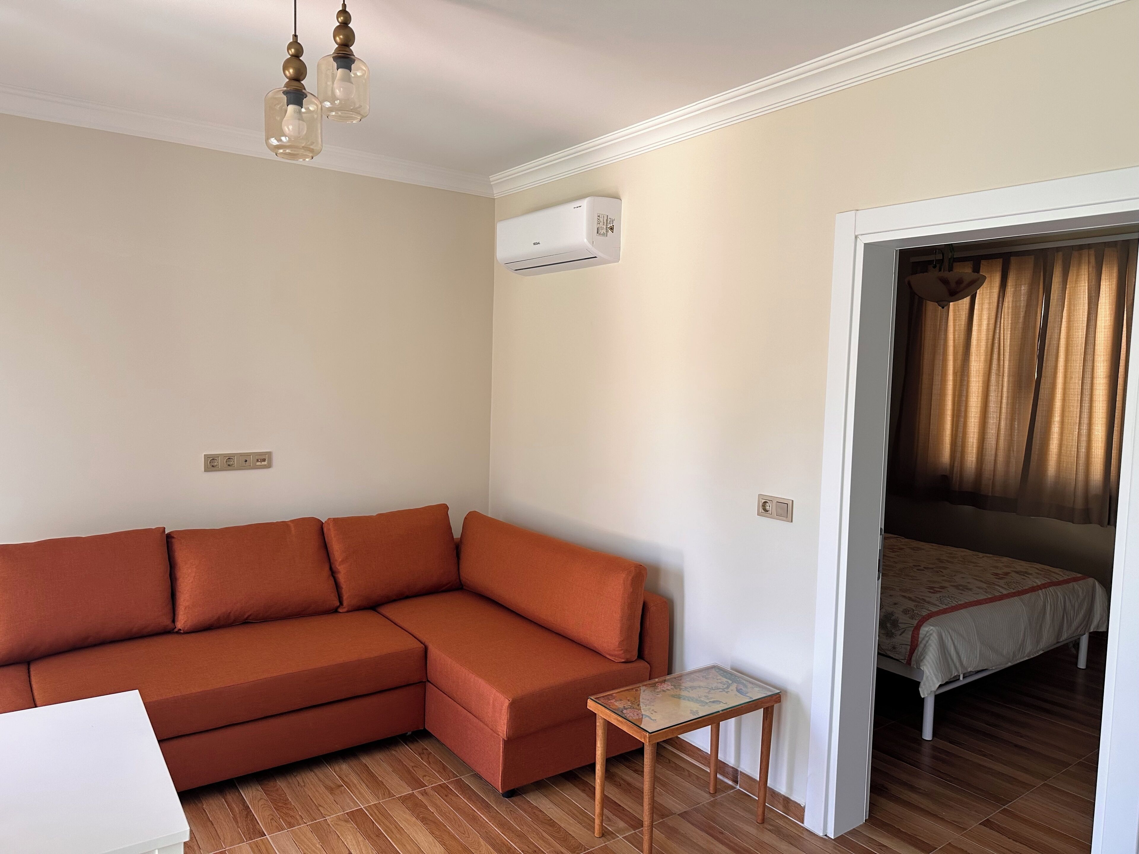 Una sala de estar con un sofá, una mesita y un equipo de aire acondicionado, con una cama en la habitación contigua.