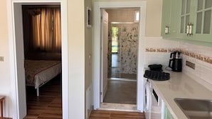 A narrow hallway leading to a bedroom with a bed, a kitchen with a coffee maker, and a bathroom with a shower.