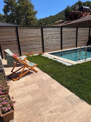 En baghave med swimmingpool, træhegn og græsplæne.