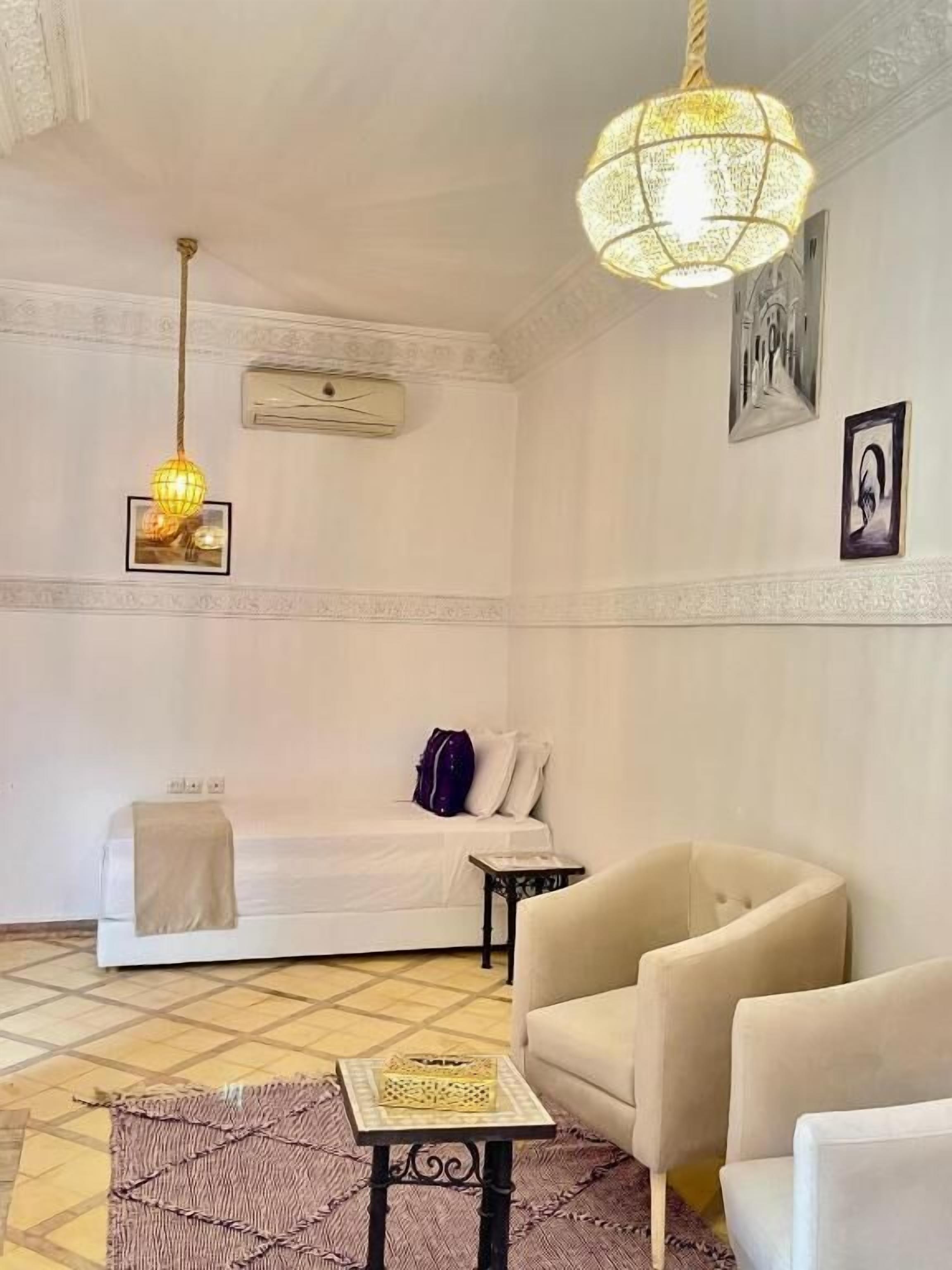 Una habitación con una cama, dos sillones, una mesita, una lámpara colgante y un aire acondicionado instalado en la pared.