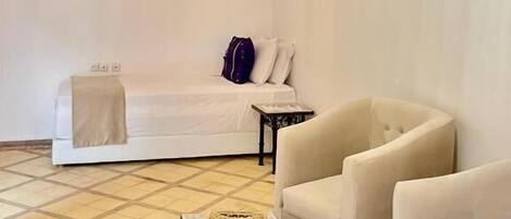 A room with a bed, two armchairs, a small table, a hanging light fixture, and a wall-mounted air conditioner.