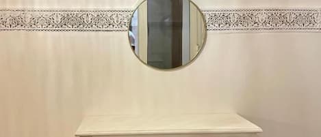 A white dresser with three drawers and a round mirror above it.