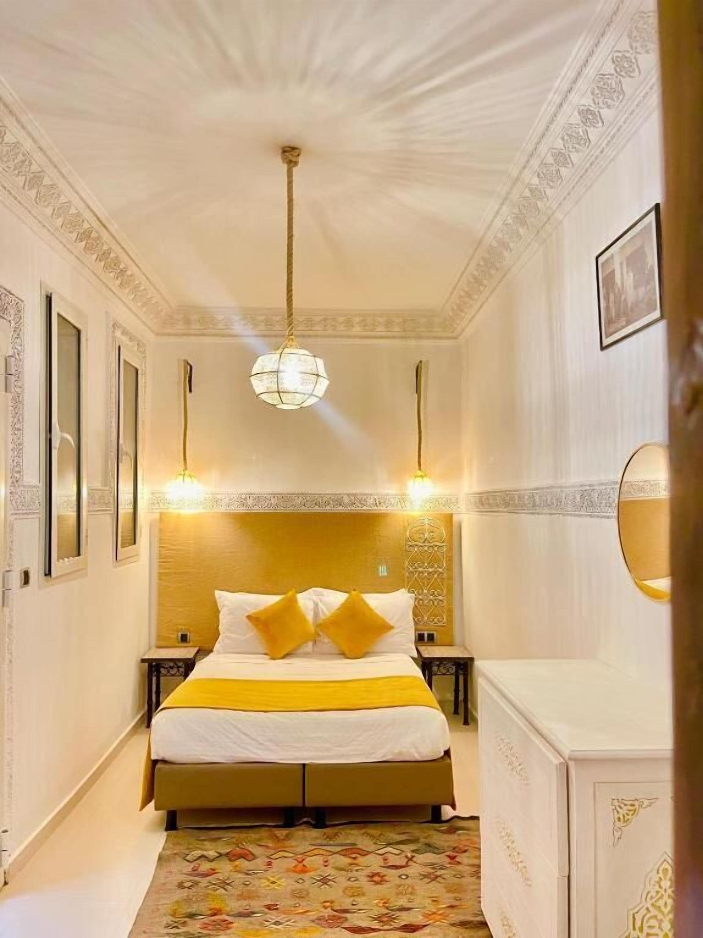 A hotel room with a bed, a chandelier, and a patterned rug.
