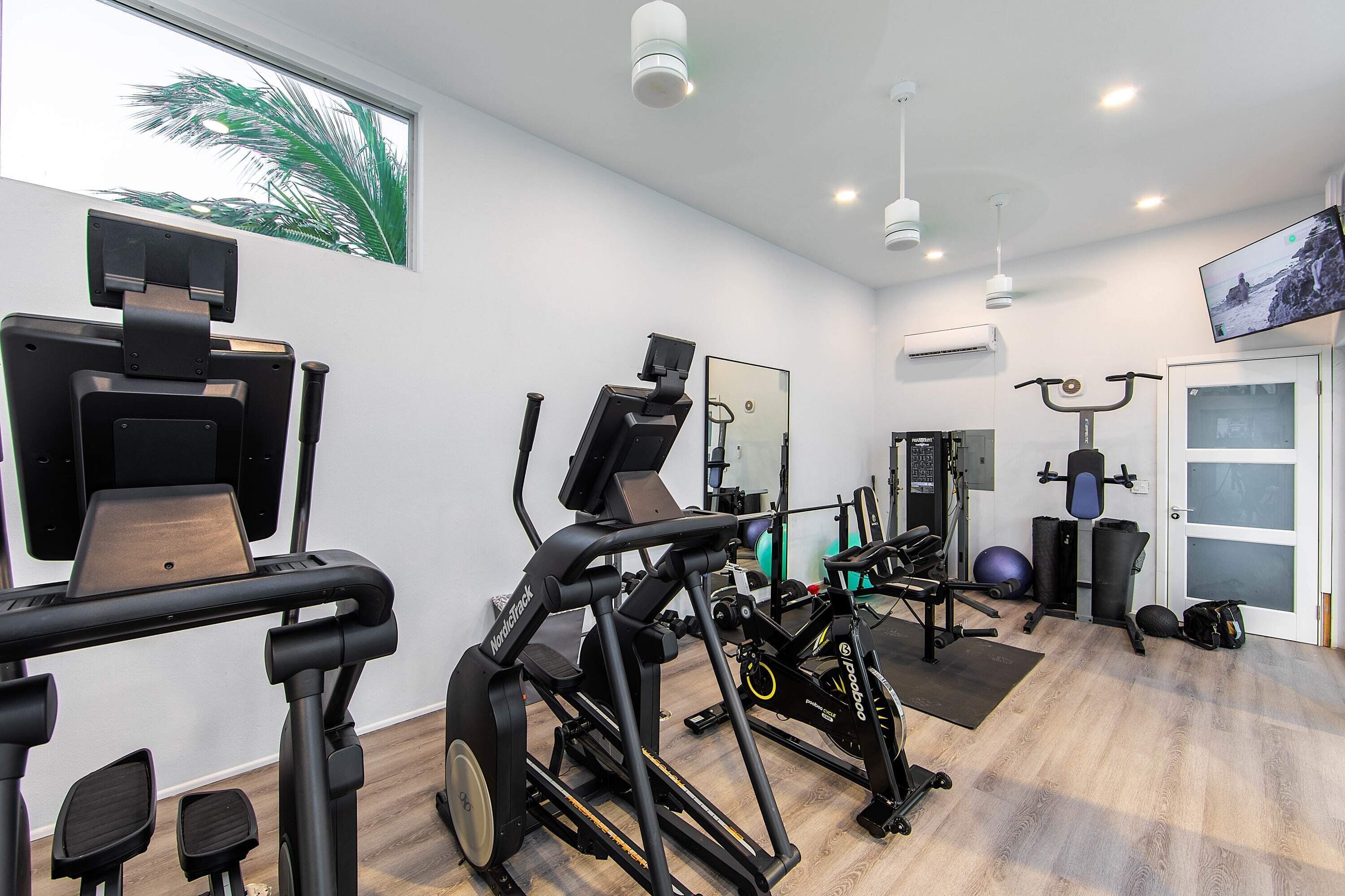 A gym with exercise equipment, a large mirror, and a TV on the wall.