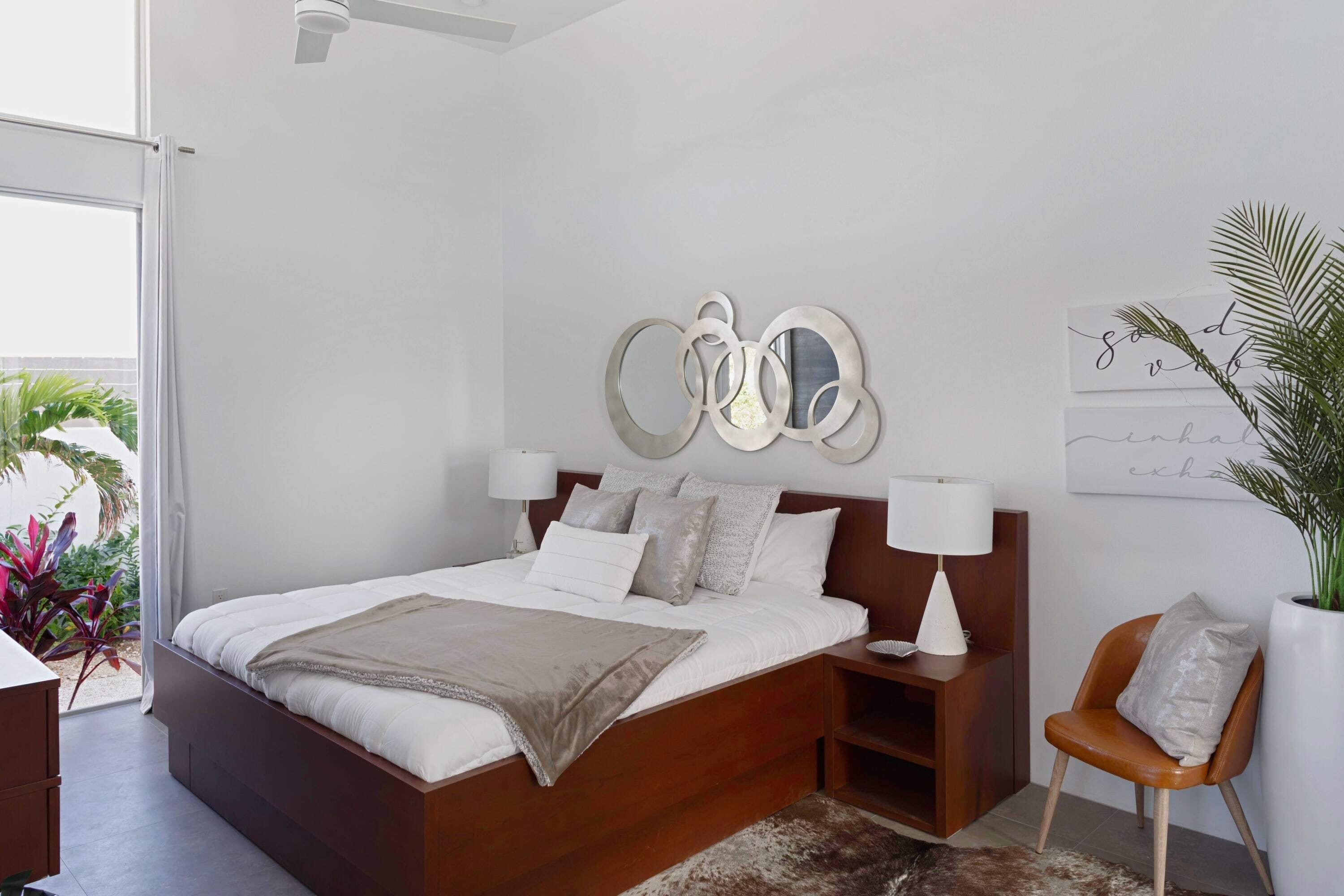 A modern bedroom with a wooden bed, bedside lamps, a decorative wall piece, and a potted plant.