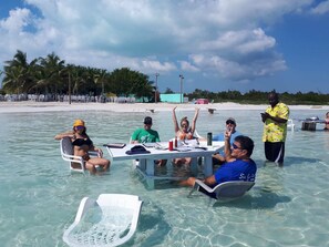 A group of people seated around a table in shallow water, with a beach and palm trees in the background. - Perfect for 1 Couple - Pool & Beach Access (Providenciales)