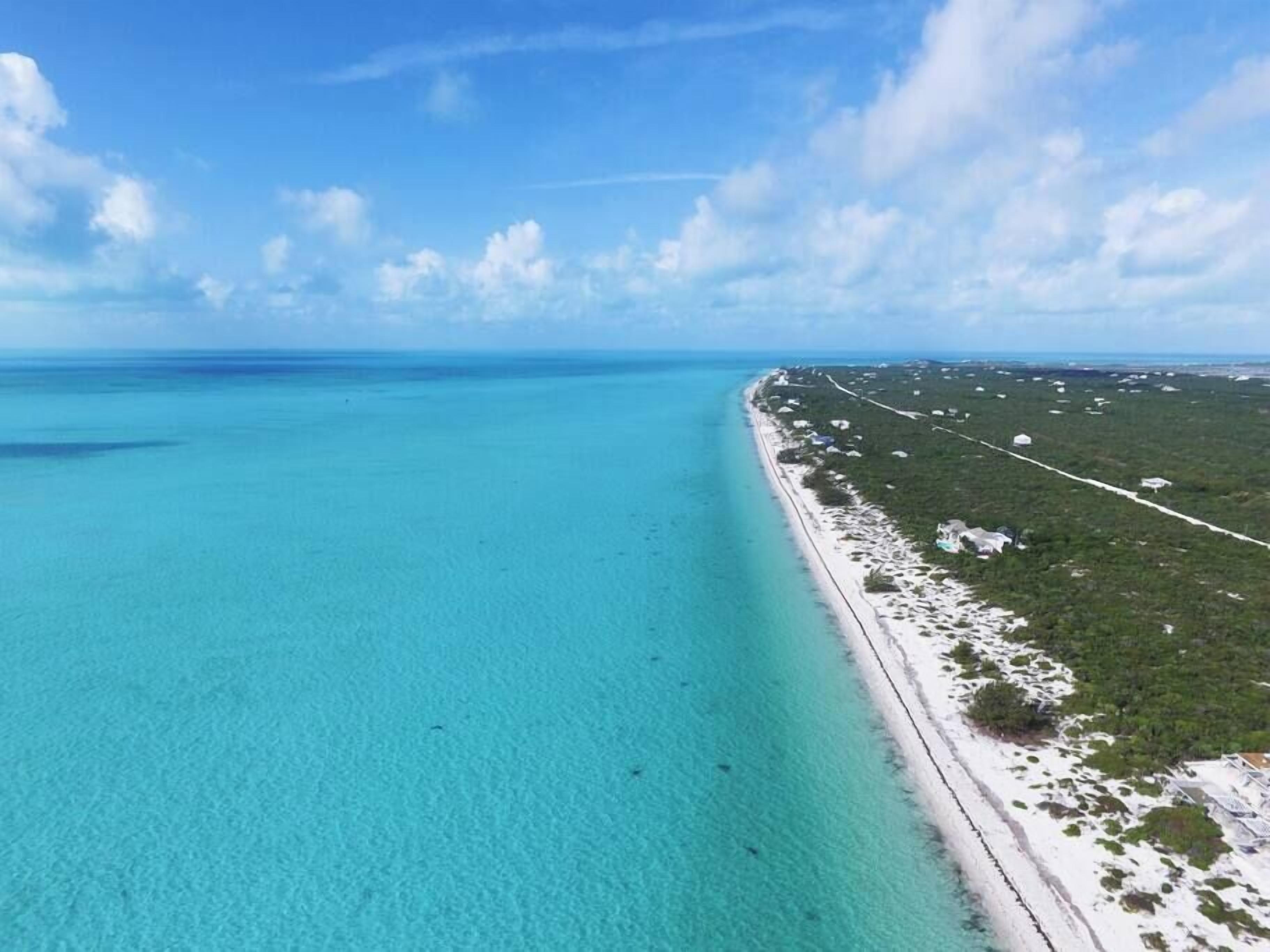 An aerial view of a beach with clear turquoise waters and a long stretch of white sand.