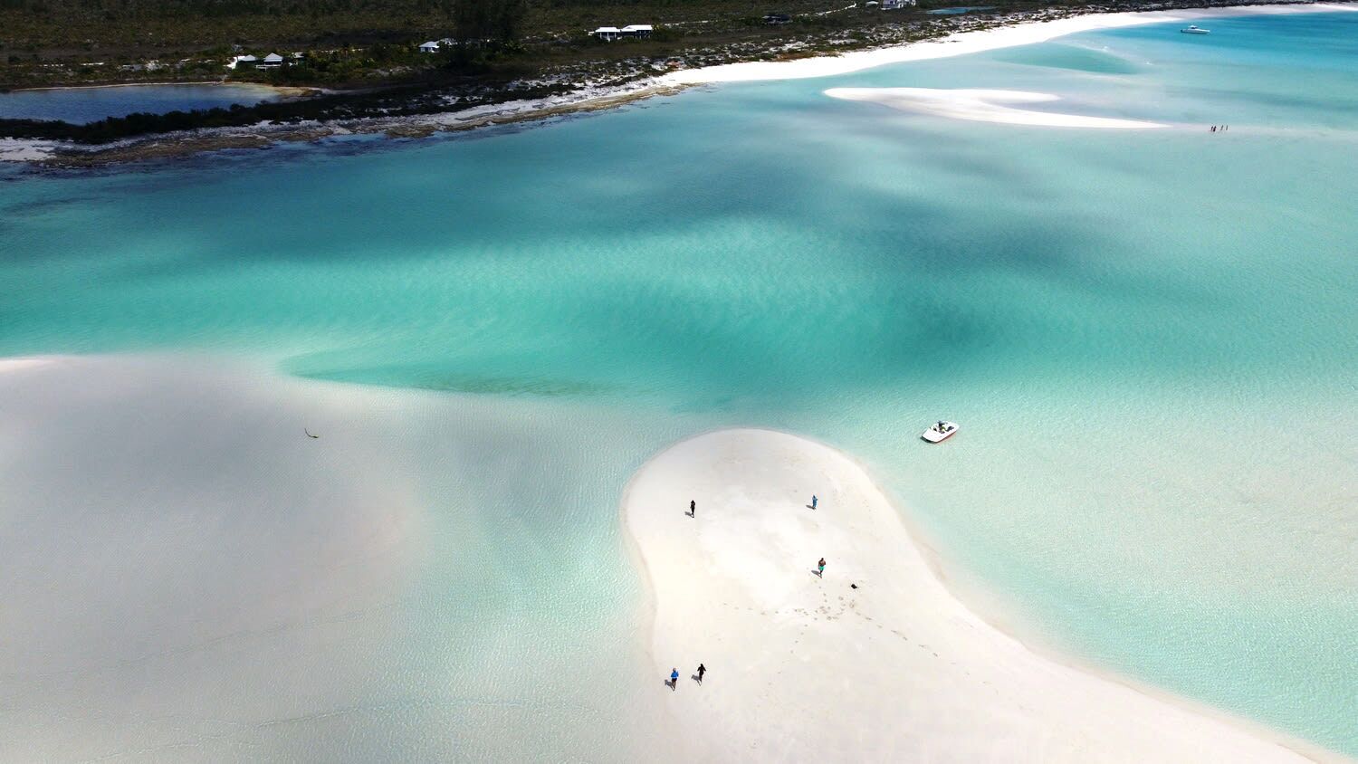An aerial view of a beach with clear turquoise waters, a sandy shore, and a few people walking.