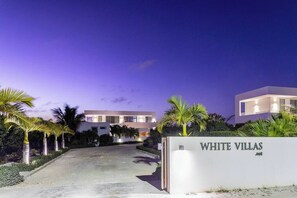 A modern villa complex with a well-lit entrance, palm trees, and a clear sky. - Perfect for 1 Couple - Pool & Beach Access (Providenciales)