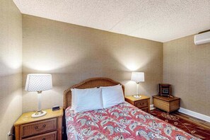 A hotel room with a bed, two bedside tables, a radio, and a wall-mounted air conditioner. - Serene 2BR Condo - POOL - FIREPLACE & Lake View (Lake Harmony)