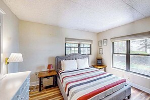 Un dormitorio con cama, mesitas de noche, lámpara, ventana y vistas al exterior.