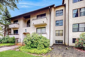 A multi-story building with balconies, a landscaped garden, and a clear sky. - Serene 2BR Condo - POOL - FIREPLACE & Lake View (Lake Harmony)