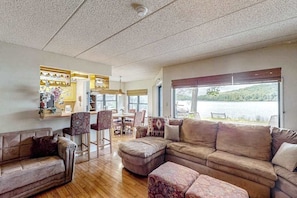 A spacious living room with a large sectional sofa, a dining area, and a kitchen with a view of a lake. - Serene 2BR Condo - POOL - FIREPLACE & Lake View (Lake Harmony)