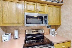 A kitchen with wooden cabinets, a stainless steel microwave, a black stove, a toaster, and a coffee maker. - Serene 2BR Condo - POOL - FIREPLACE & Lake View (Lake Harmony)