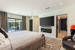 Una camera da letto moderna con un letto grande, una televisione a schermo piatto e una porta scorrevole in vetro che dà su un balcone.