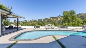 Una piscina con lettini e una zona relax coperta, immersa nel verde con colline sullo sfondo.