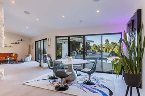 Un soggiorno moderno con vista piscina, un'area pranzo con sedie e un divano.
