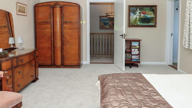 A bedroom with a large wooden wardrobe, a bed with a brown quilt, a dresser, a mirror, a painting, and a bookshelf. - The White House (Okehampton)