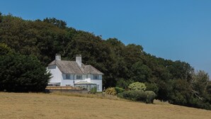 A white house with a gabled roof, surrounded by a grassy field and dense trees. - The White House (Okehampton)