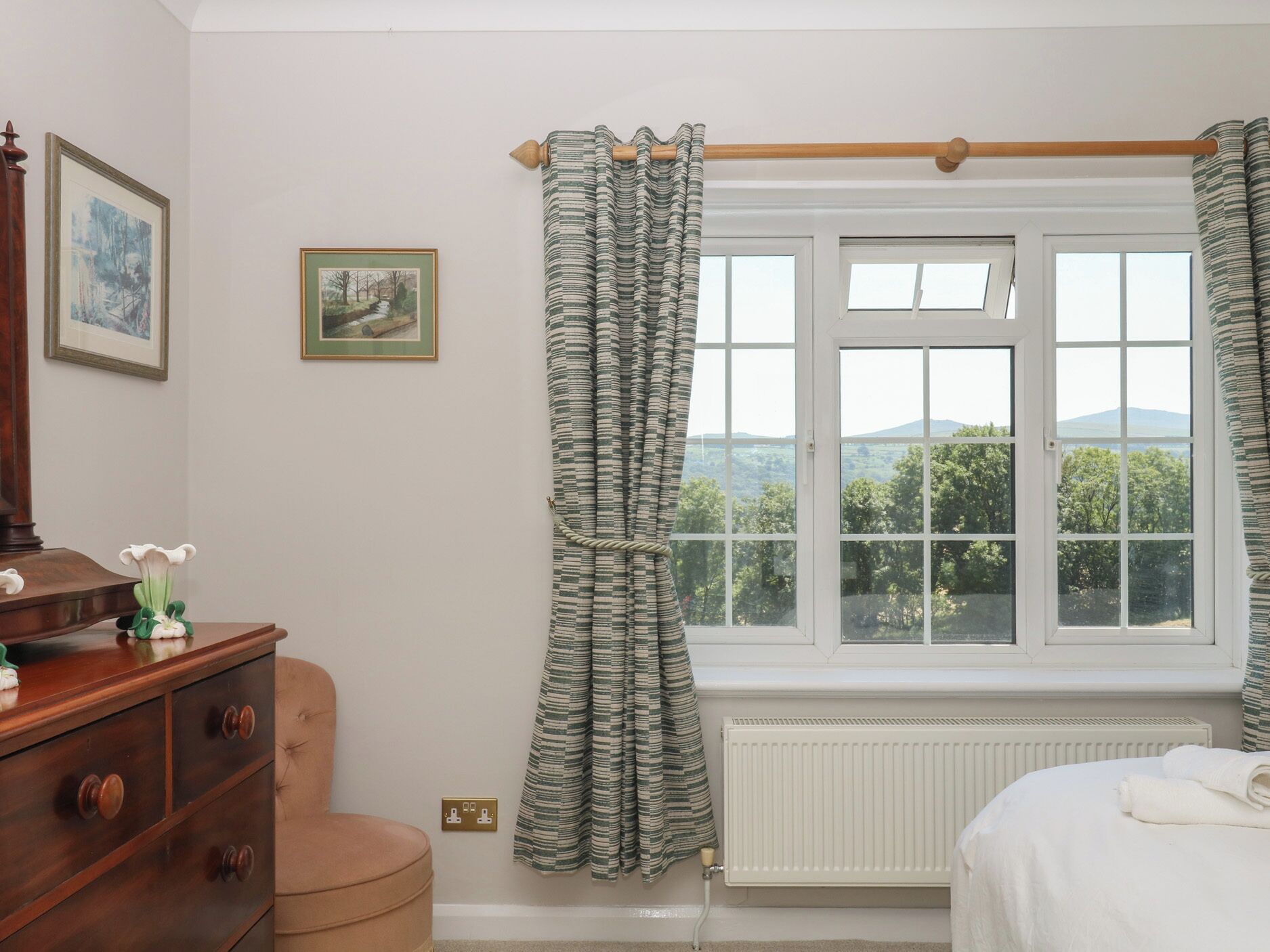 A bedroom with a window, a radiator, a wooden dresser, and a bed.